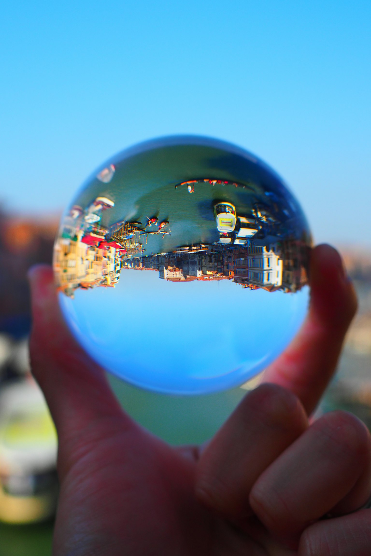 Eine klare Glaskugel, die in der Hand gehalten wird und den blauen Himmel und die Stadtlandschaft reflektiert