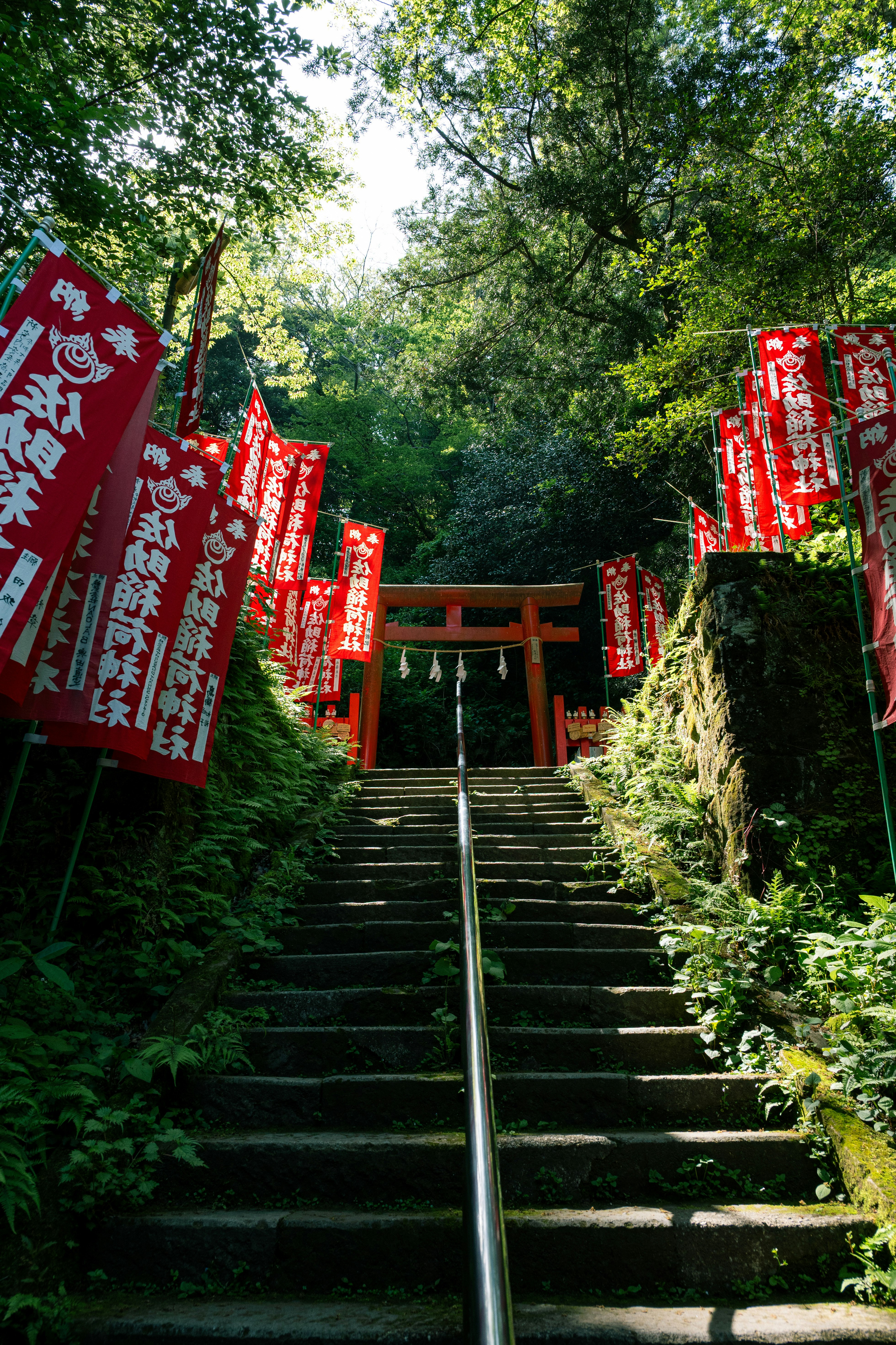 緑に囲まれた石段の参道と赤い幟のある神社の入口