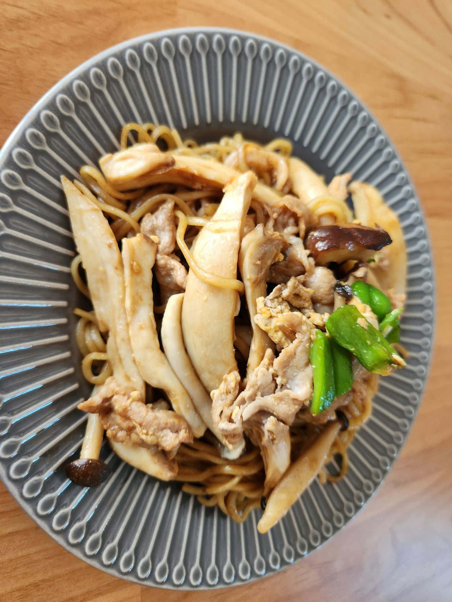 Gebratenes Hähnchen mit weißen Nudeln und Frühlingszwiebeln auf einem gemusterten Teller