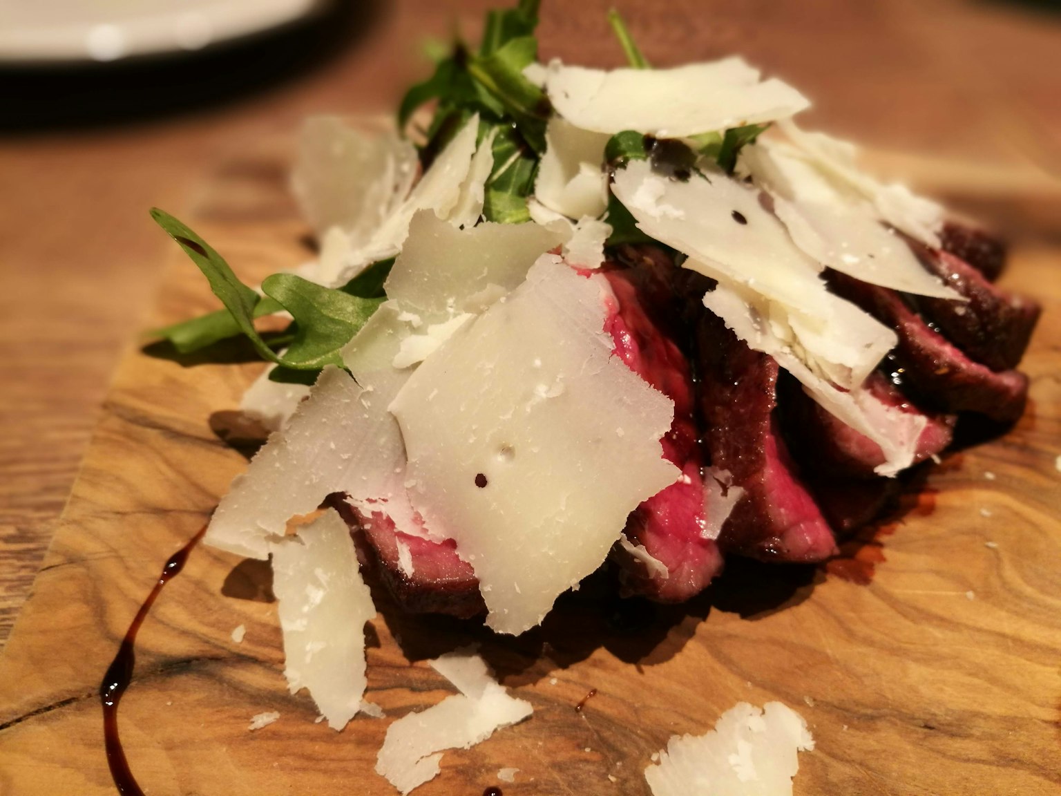 In Scheiben geschnittenes Fleisch auf einem Holzbrett mit frischen Kräutern und gehobeltem Parmesan