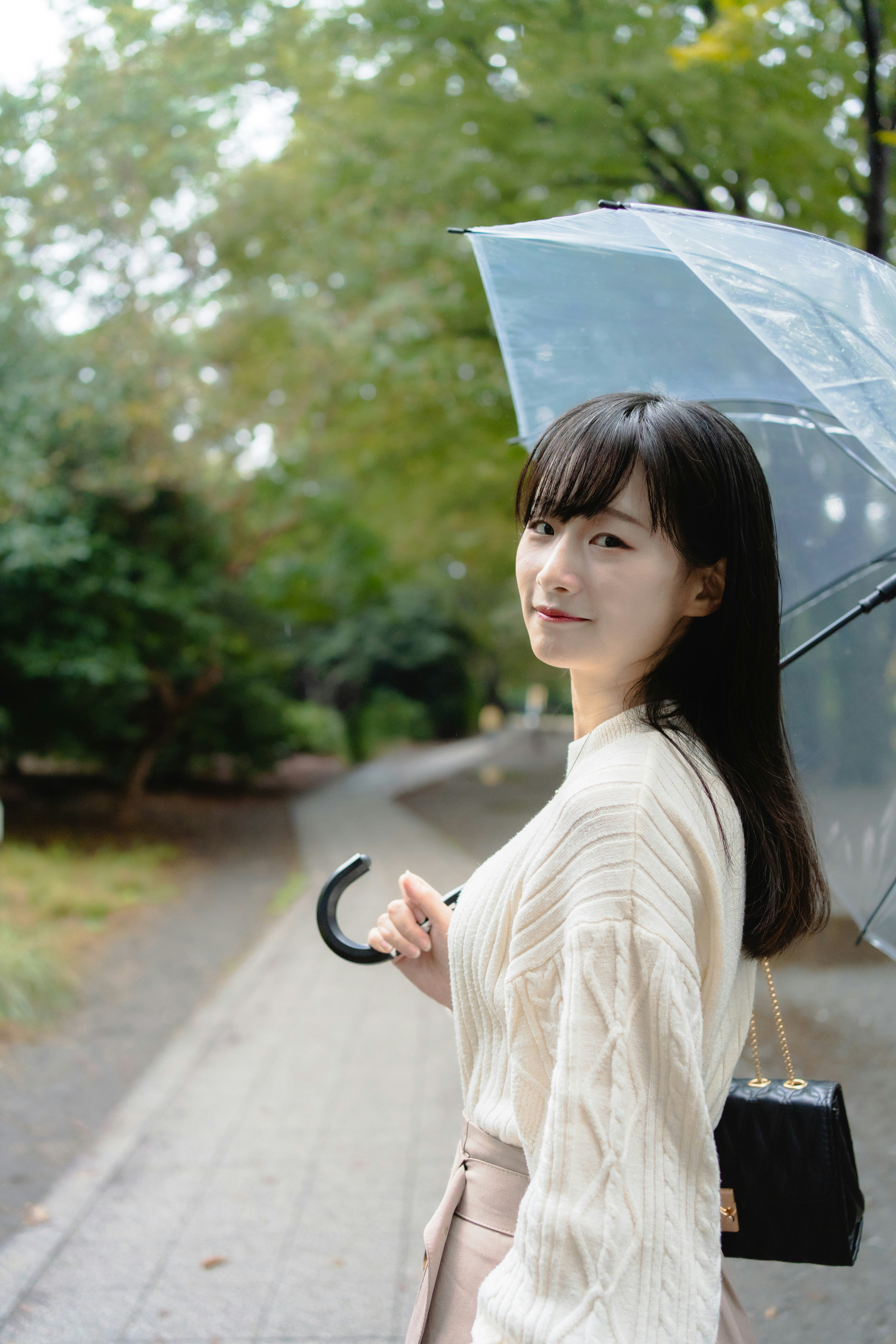 緑の並木道で傘を持つ女性の振り返る日常の一瞬