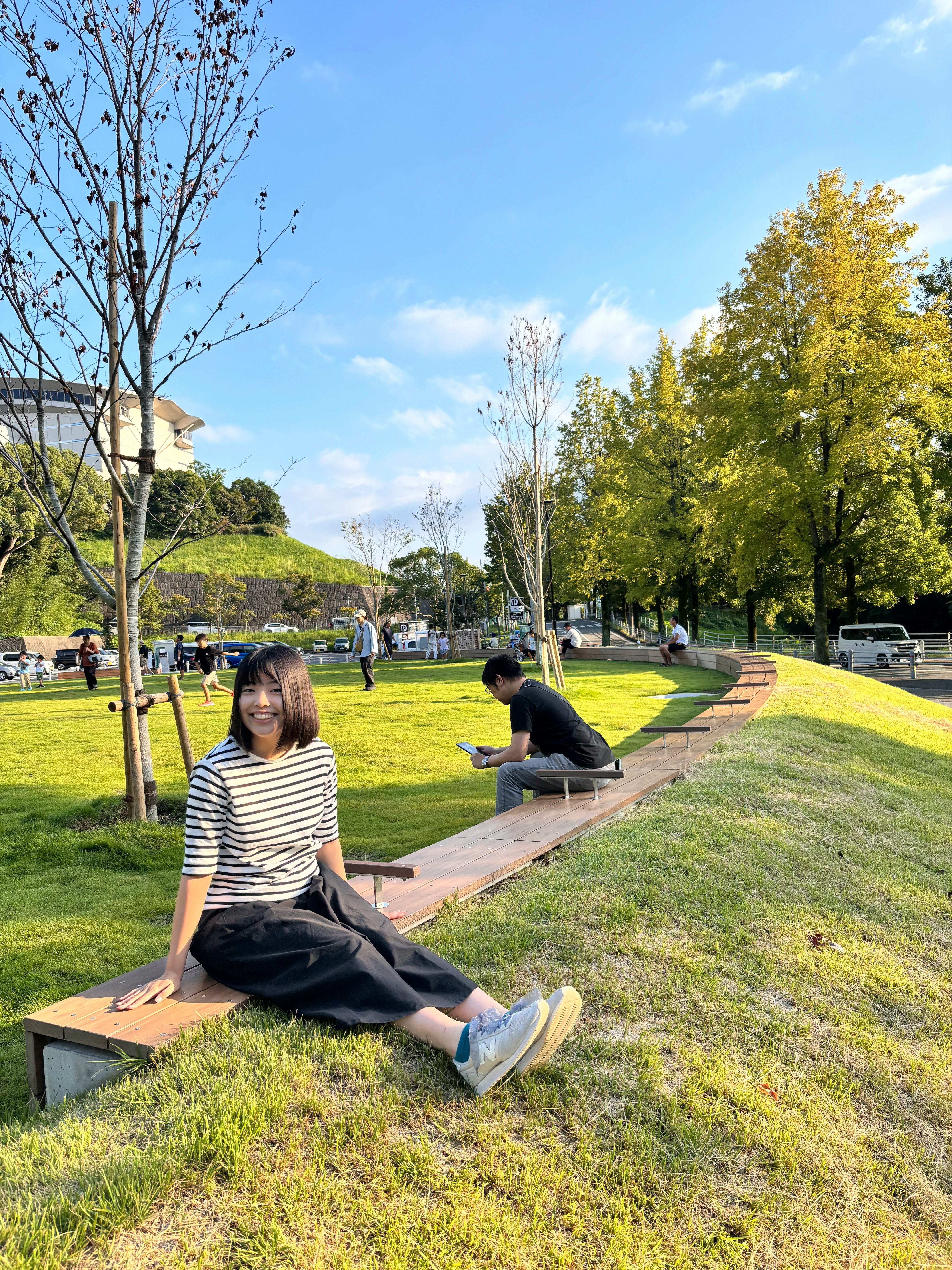 芝生の公園でベンチに座る人物と散歩する人々のある風景