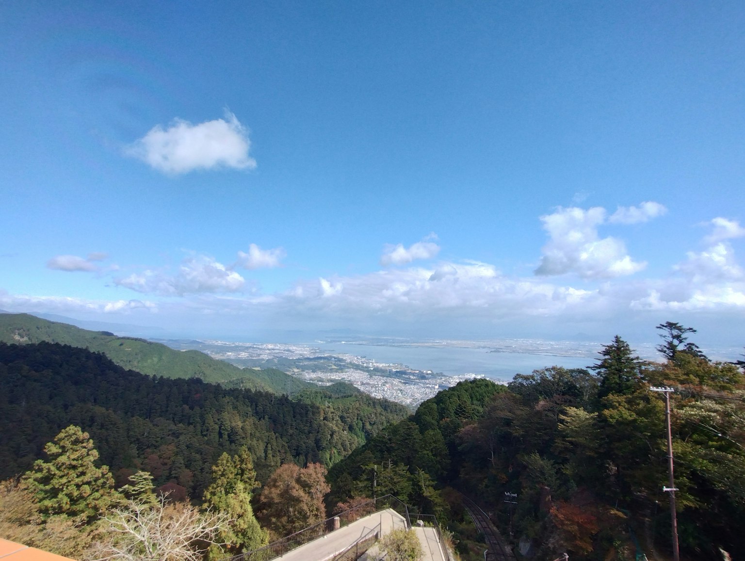 Vue de montagne avec ciel bleu et nuages présentant une végétation luxuriante et un paysage urbain lointain