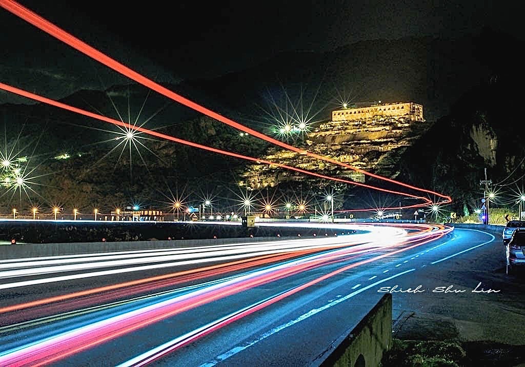 夜の道路に流れる車の光と背景にある山の上の建物