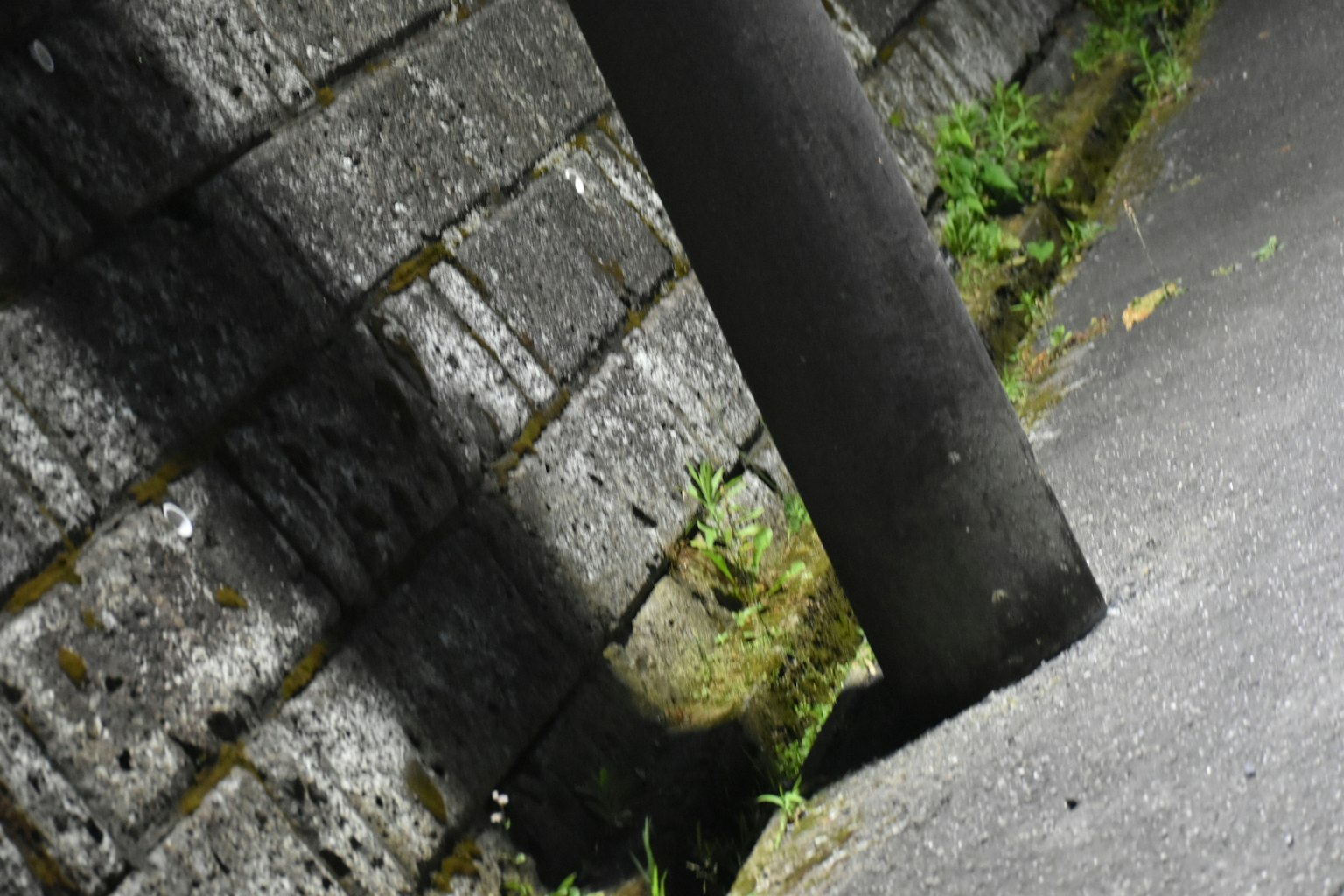 Eckpfahl wirft Schatten auf eine Steinmauer in einem schwach beleuchteten Weg