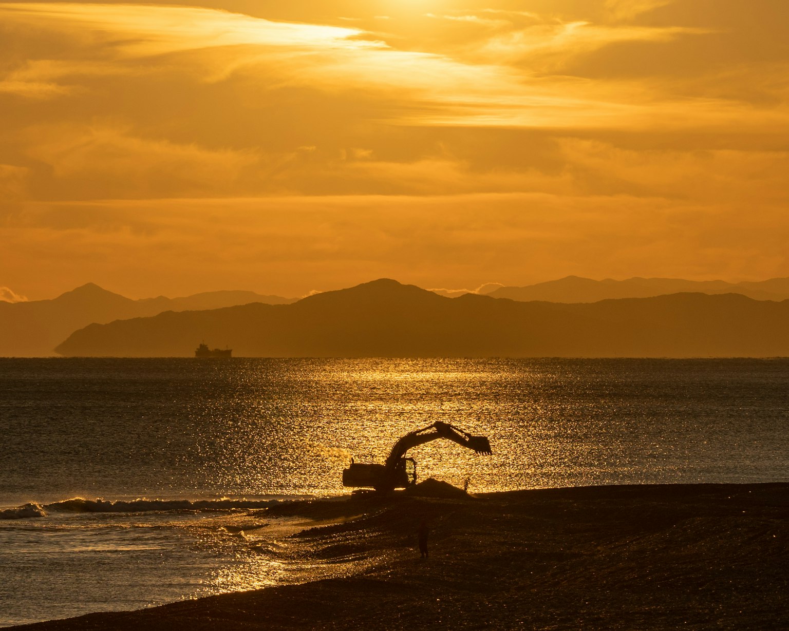 Silhouette eines Baggers, der am Strand bei Sonnenuntergang arbeitet