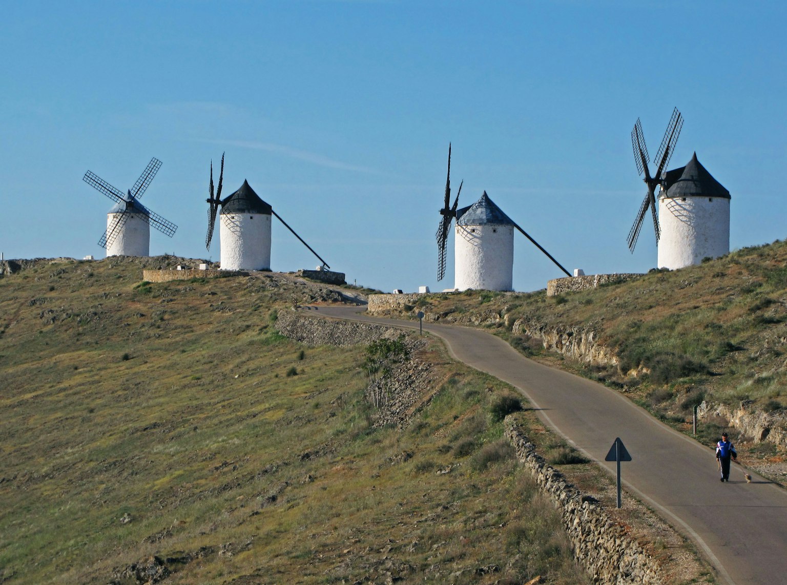 Paisaje con molinos de viento bajo un cielo despejado una persona caminando por un camino