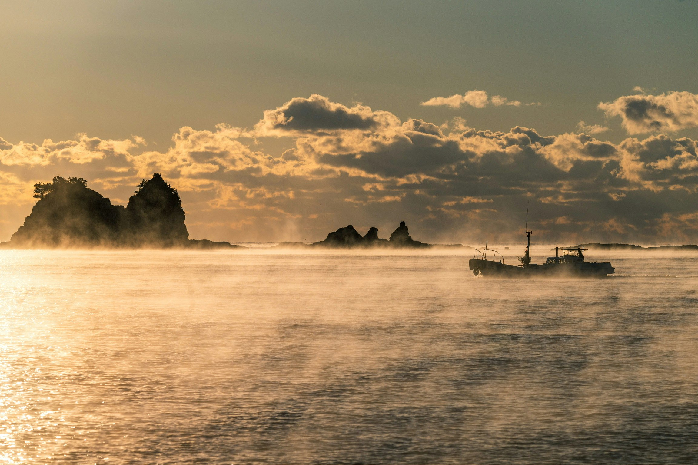 海霧の中、夕日に照らされる渡船と海面の風景
