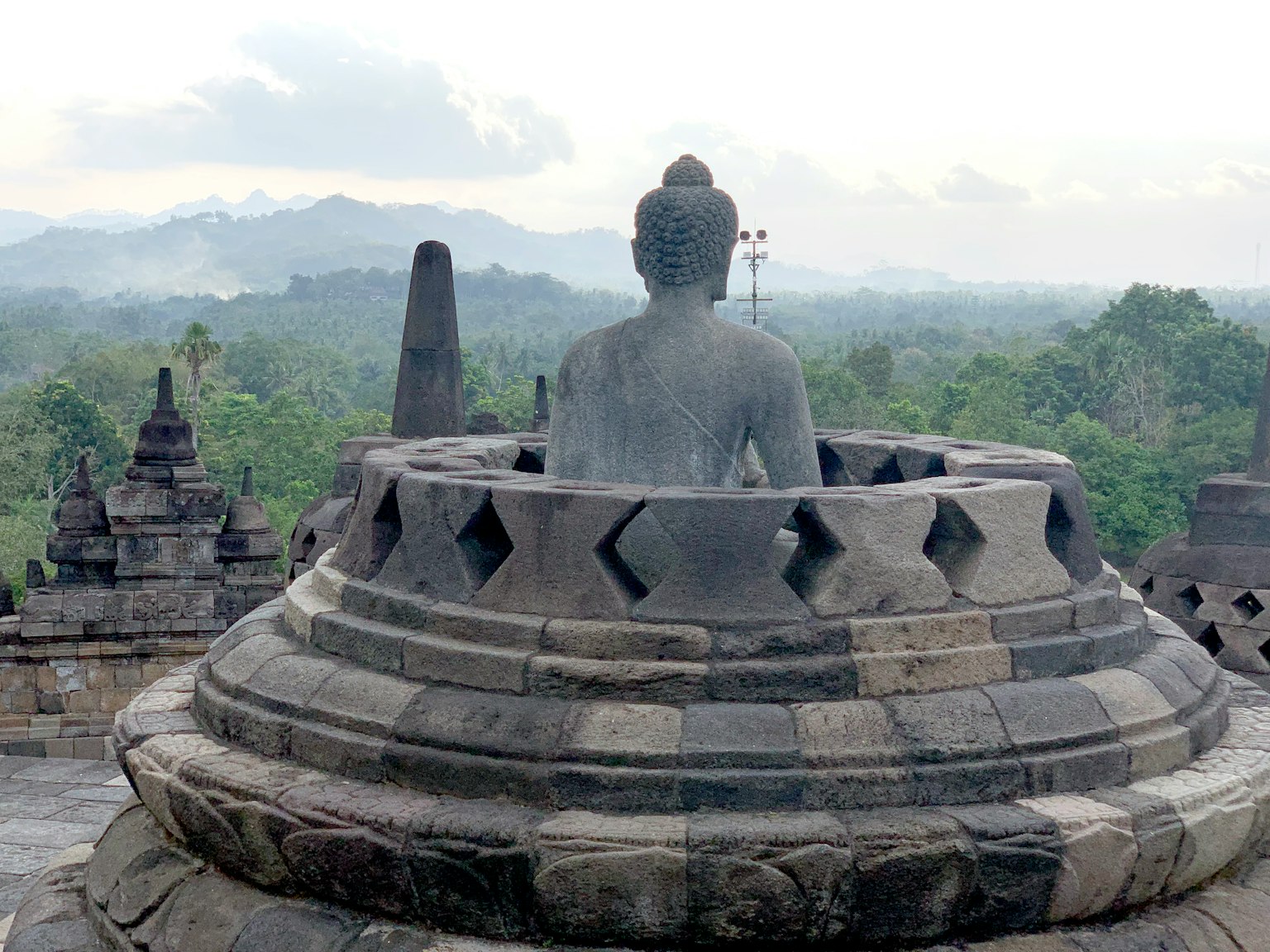 มุมมองด้านหลังของรูปปั้นพระพุทธเจ้า ณ วัดโบโรบูดูร์ พร้อมภูมิทัศน์ที่เขียวขจีในพื้นหลัง