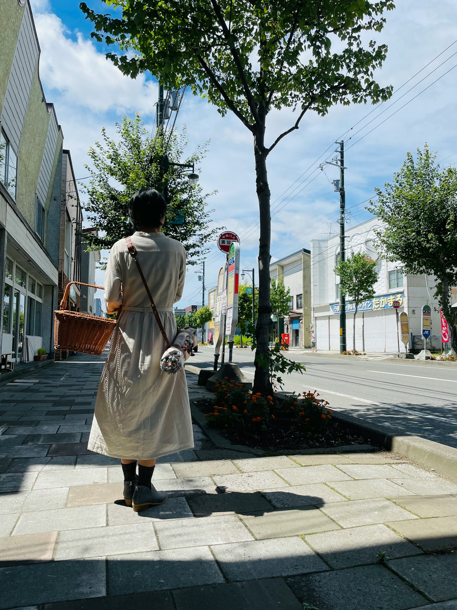 Donna che cammina in una strada cittadina con un cappotto beige cielo blu e alberi verdi