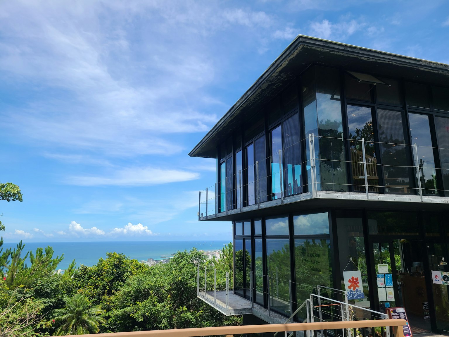 現代玻璃建築，背景是海景和郁郁蔥蔥的綠地