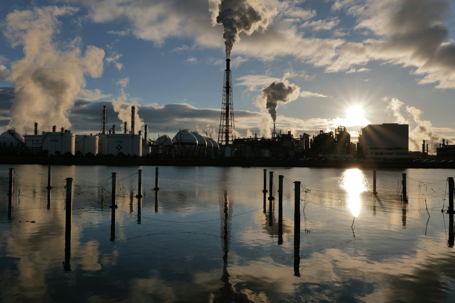 Paysage industriel avec de la fumée s'élevant des cheminées se reflétant dans l'eau au coucher du soleil