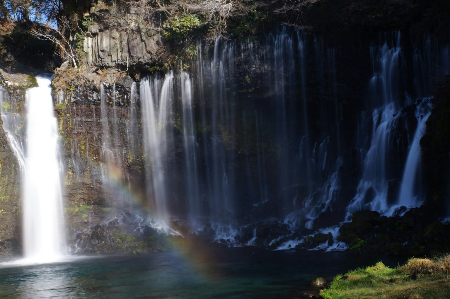 Air terjun yang indah dengan pelangi di tepi air yang tenang