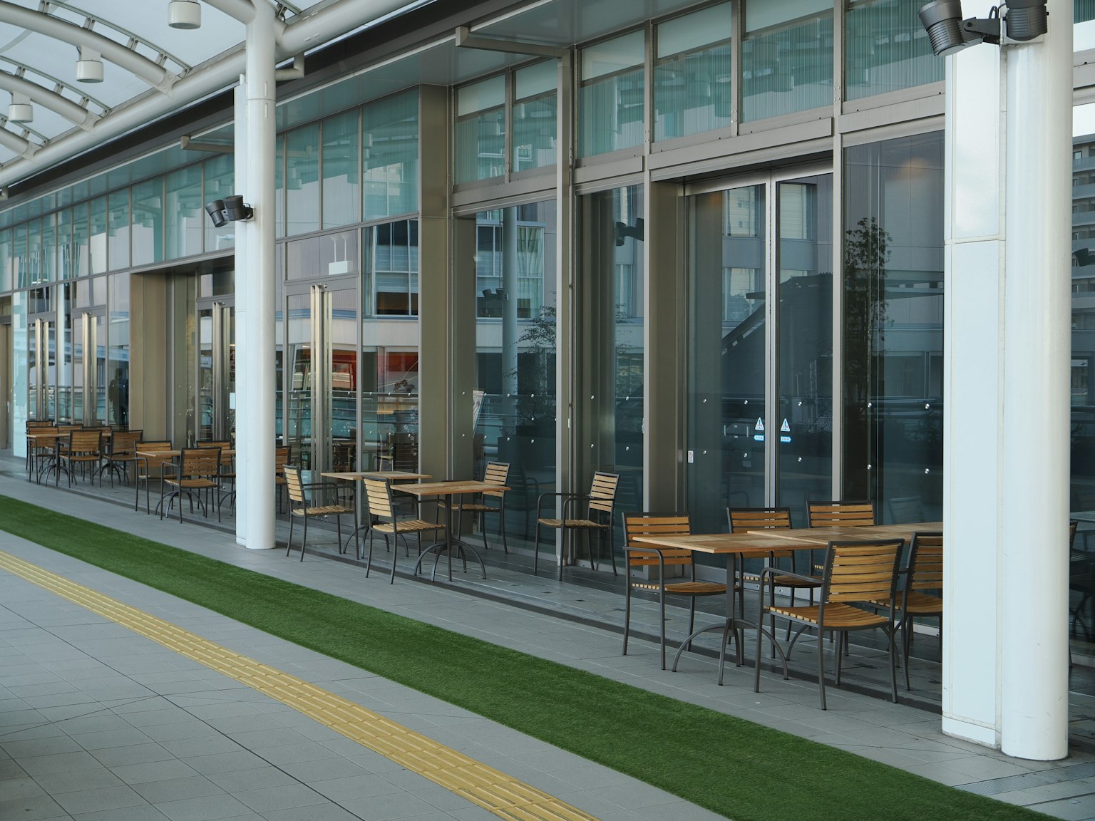 Terraza de café moderna con mesas y sillas de madera contra paredes de vidrio
