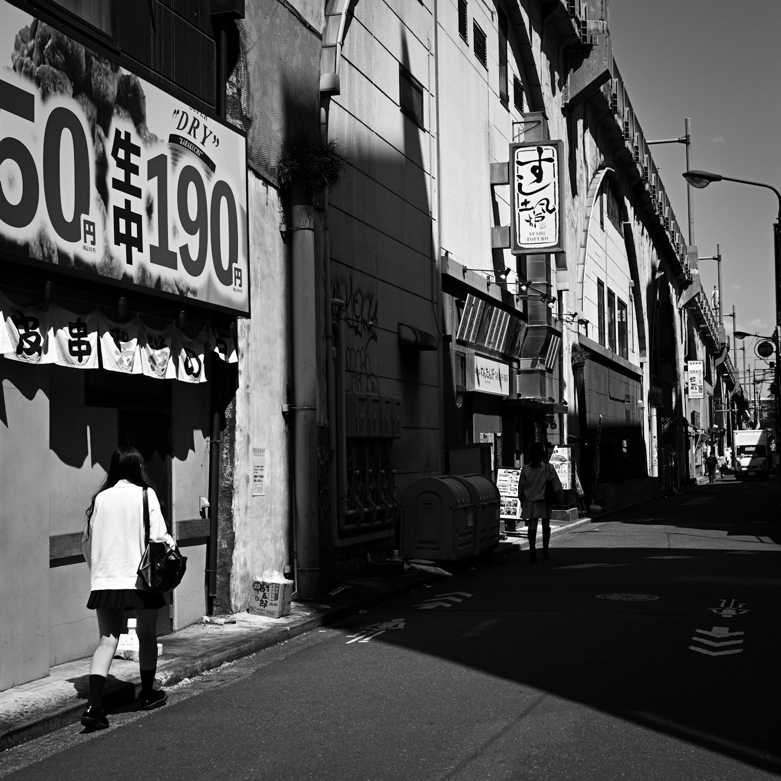 Escena de calle en blanco y negro con peatones y letreros de tiendas en un callejón