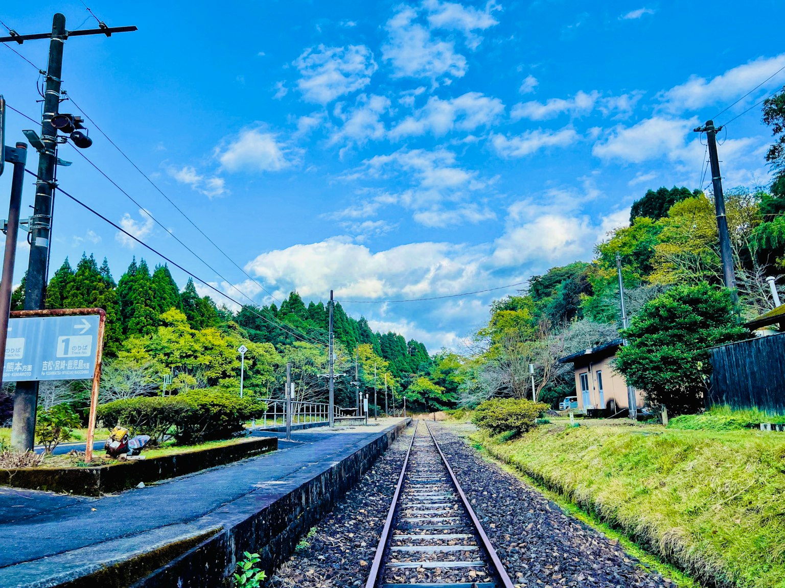 Vista panoramica di una tranquilla stazione ferroviaria circondata da montagne verdi e cielo blu