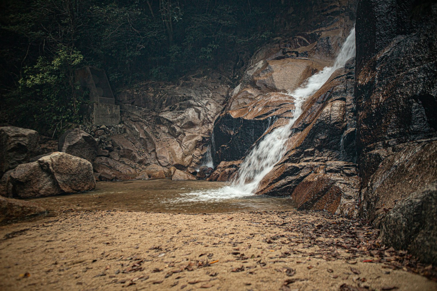 Ruhige Szene eines Wasserfalls umgeben von Felsen und einem Sandstrand