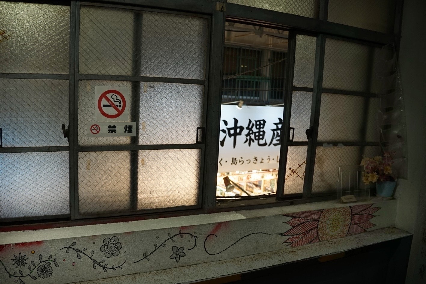 Innenansicht eines alten Gebäudes mit einem Schild für Okinawa und einem Nichtraucher-Schild, das durch ein Fenster sichtbar ist