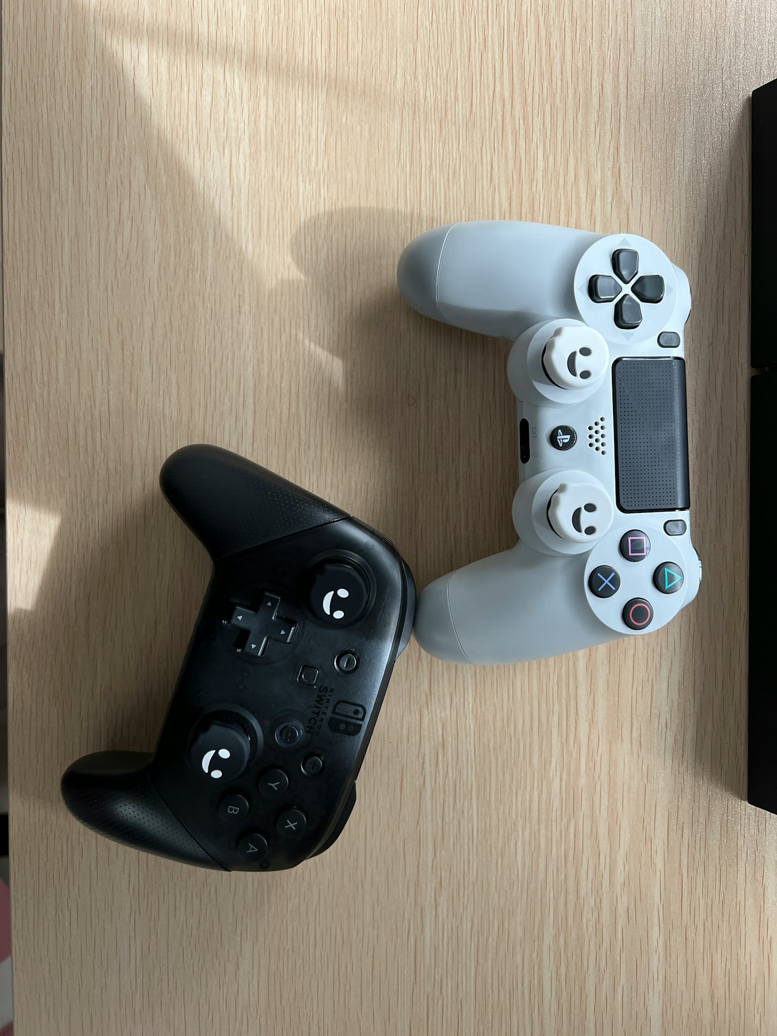 Bộ điều khiển Xbox đen và bộ điều khiển PlayStation trắng đặt trên bàn gỗ