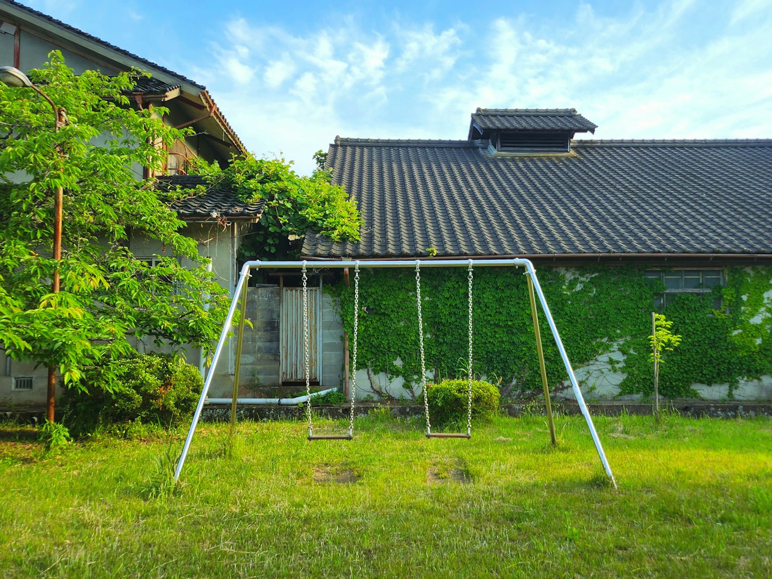 Balançoires dans un jardin envahi par la végétation avec une maison ancienne