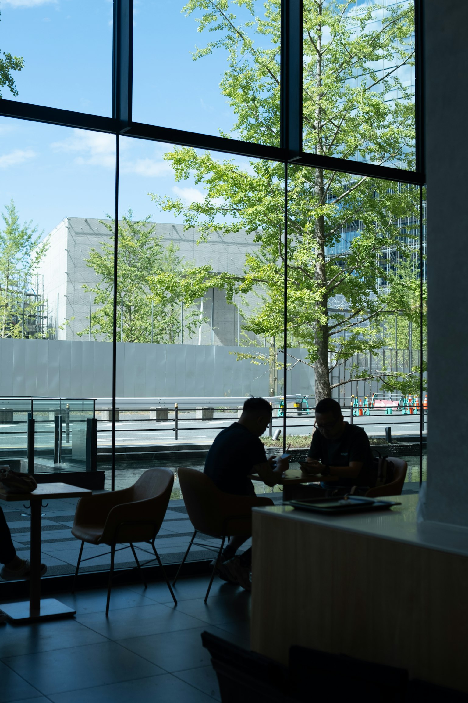 Deux personnes assises dans un café lumineux regardant à travers de grandes fenêtres avec des arbres verts à l'extérieur
