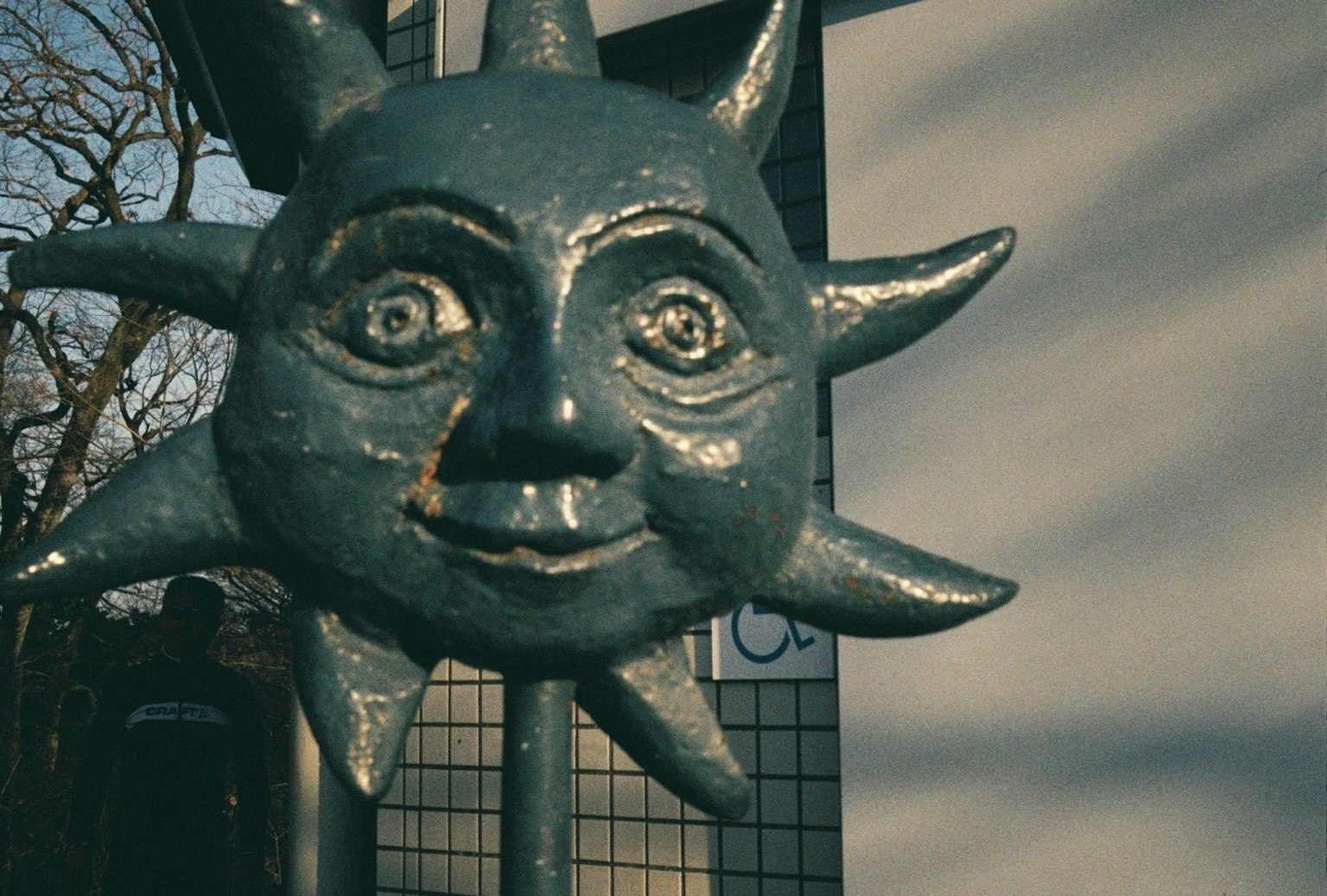 Sculpture métallique d'un visage de soleil avec des rayons et un arrière-plan flou