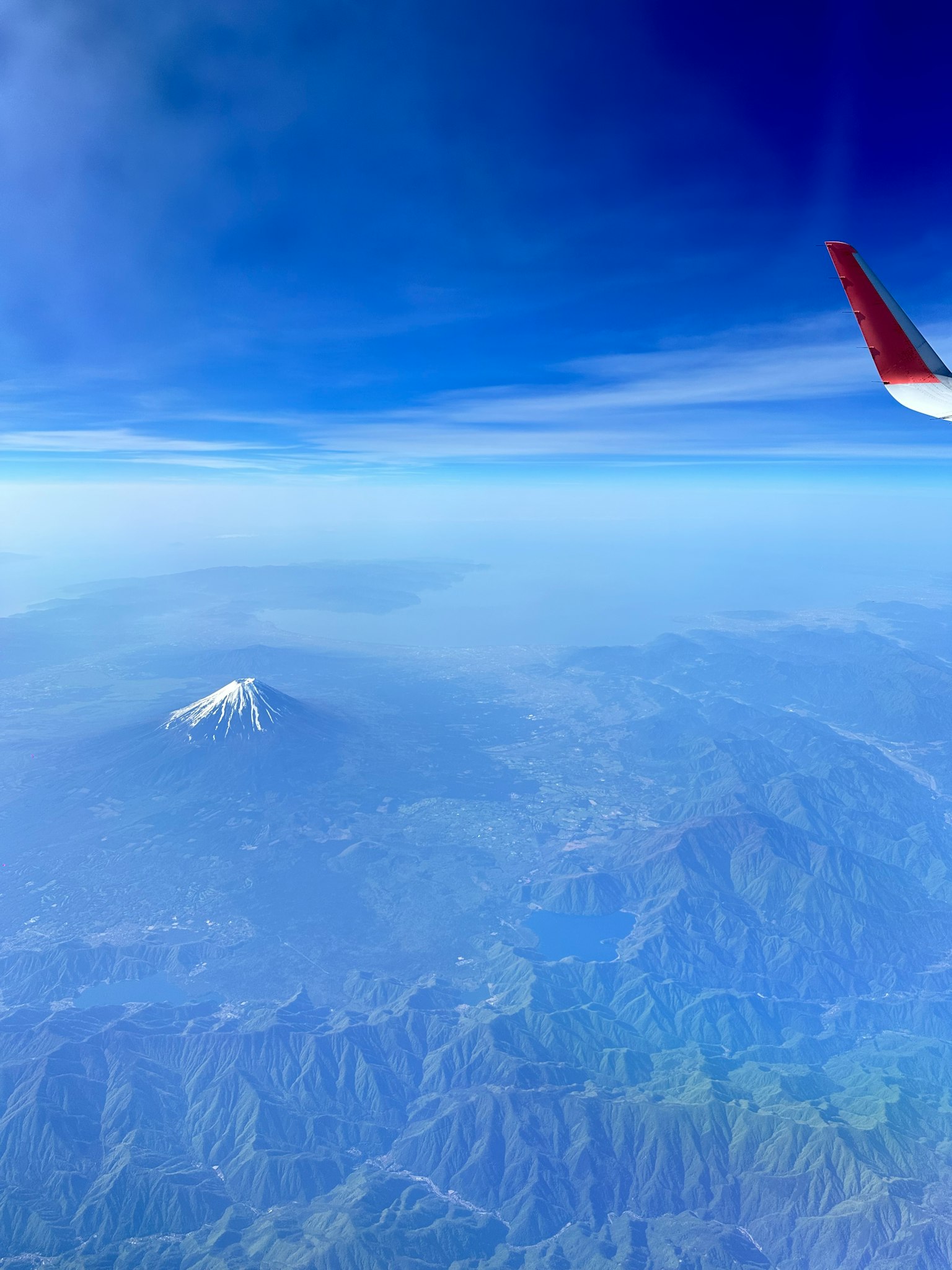 Schneebedeckter Berg von einem Flugzeugfenster mit blauem Himmel aus gesehen
