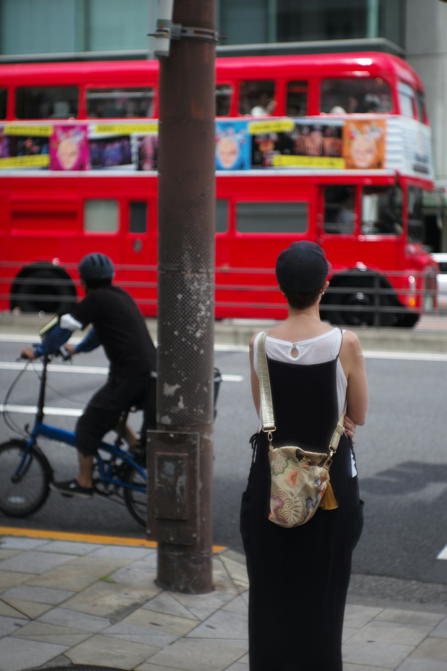 Wanita berdiri dengan bus dua lantai merah dan pengendara sepeda di latar belakang