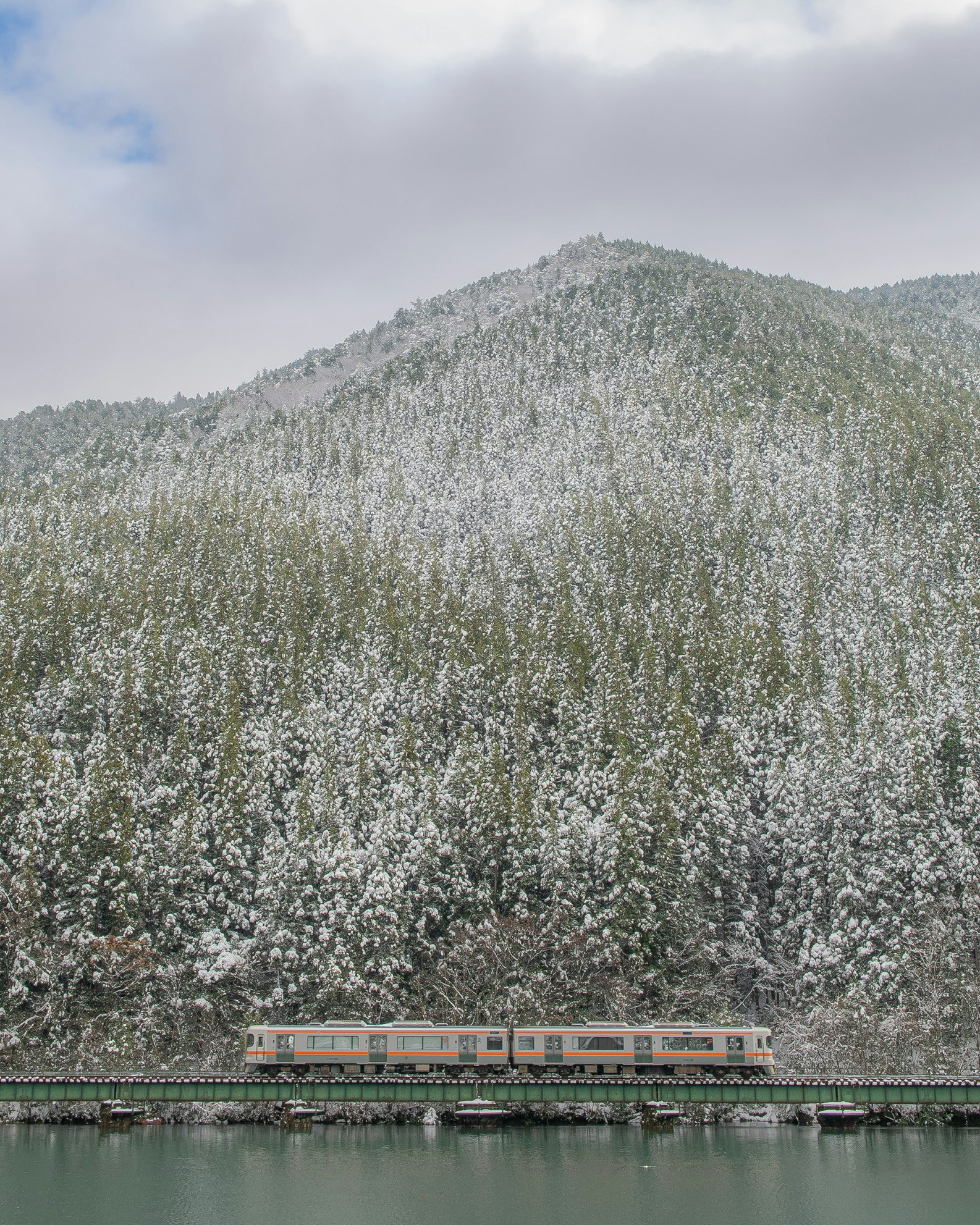 高山本線を走る列車と雪の山並みの湖畔