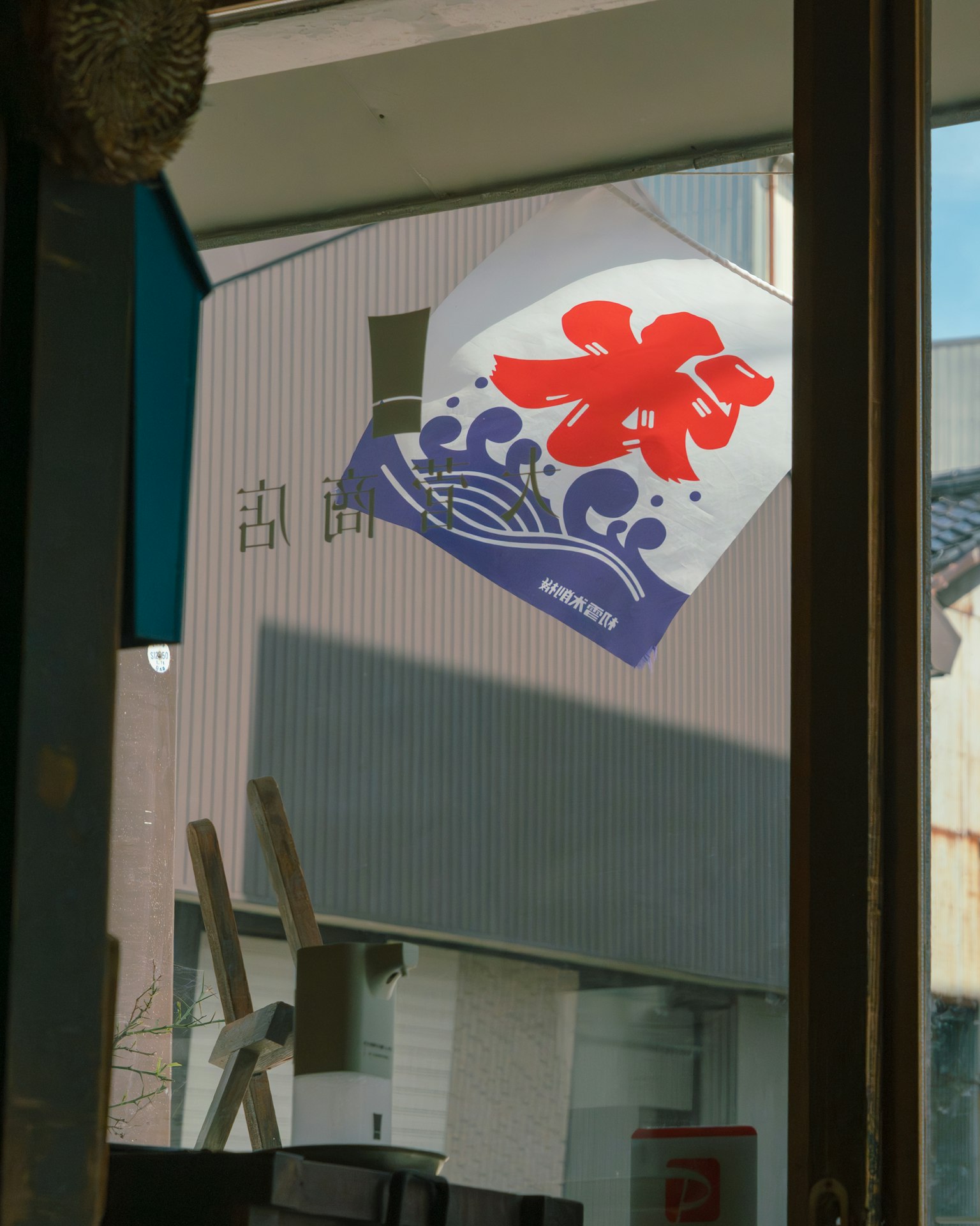 赤い花模様と波のデザインが描かれた看板が映る窓の内部