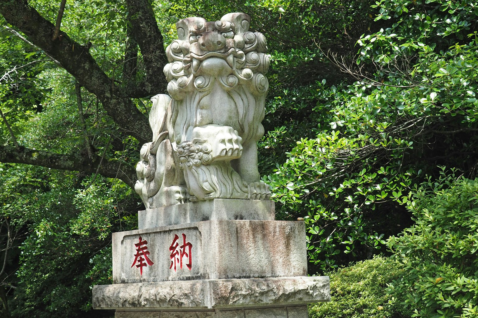 Statua di leone in pietra che si erge tra alberi verdi