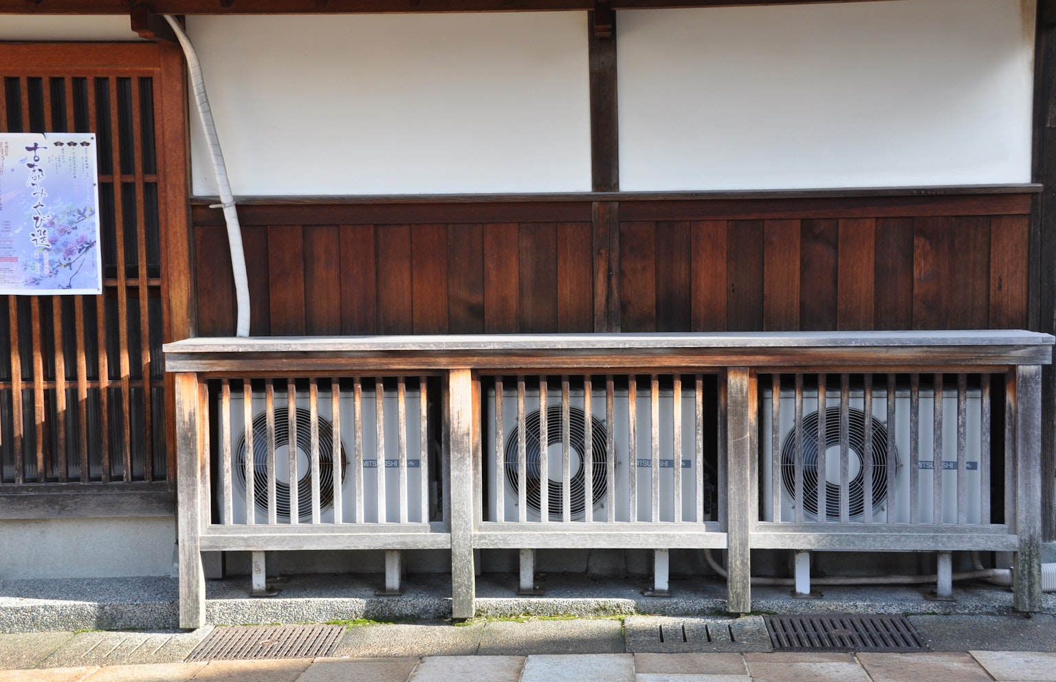 Exterior of a traditional Japanese building featuring air conditioning units behind a wooden fence