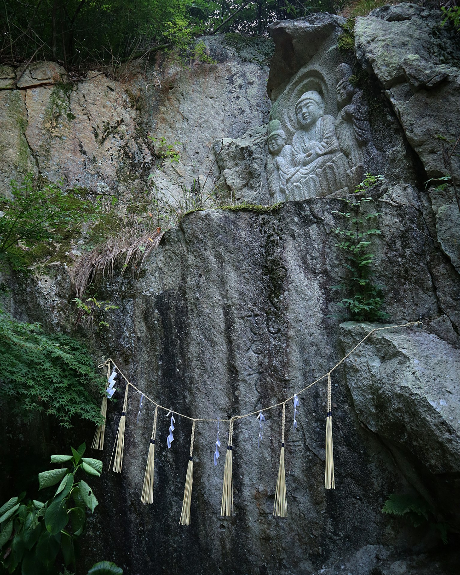 Felsen mit Buddha-Skulptur und hängenden Bambusdekorationen in einer natürlichen Umgebung