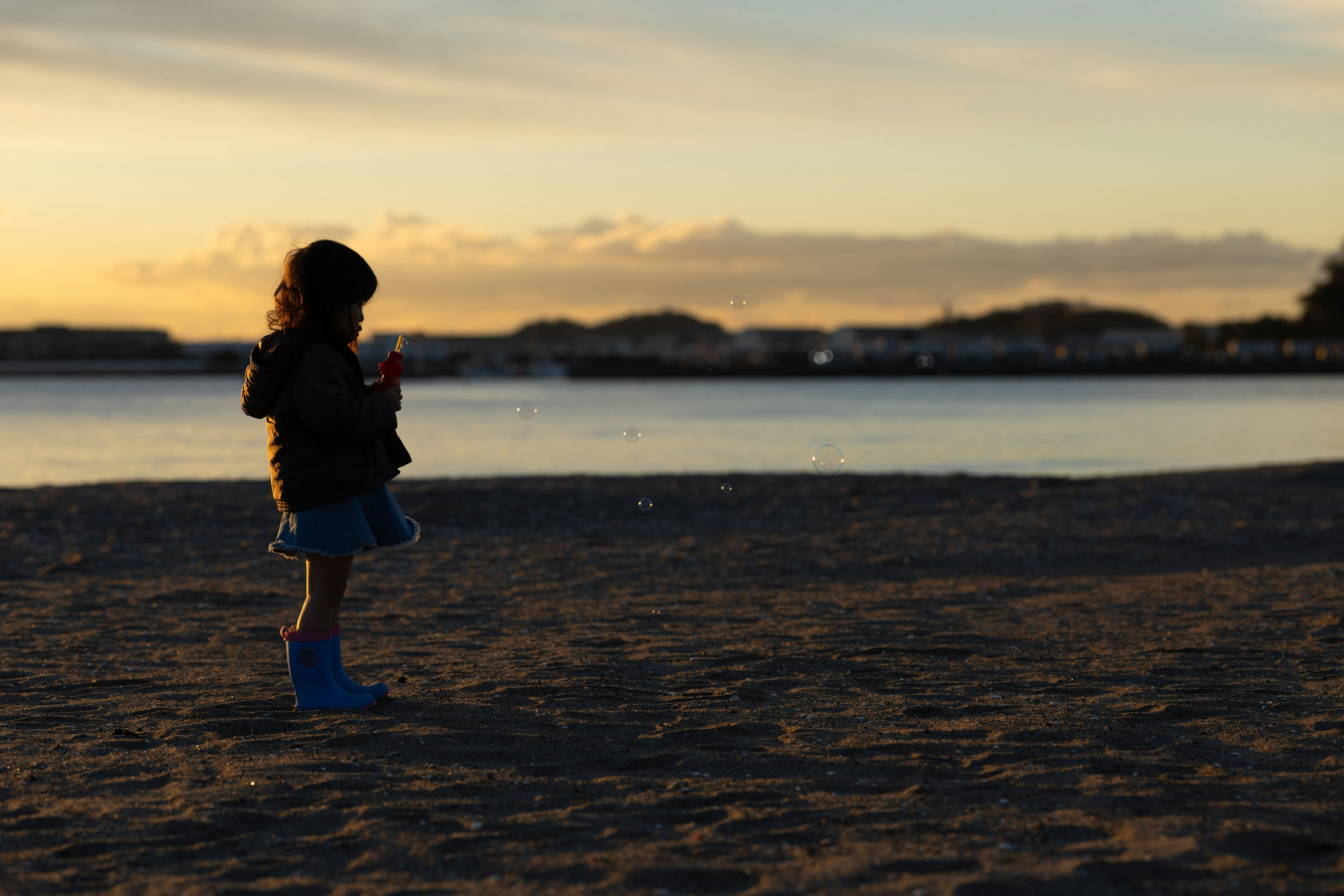 夕暮れの海辺で立つ子ども