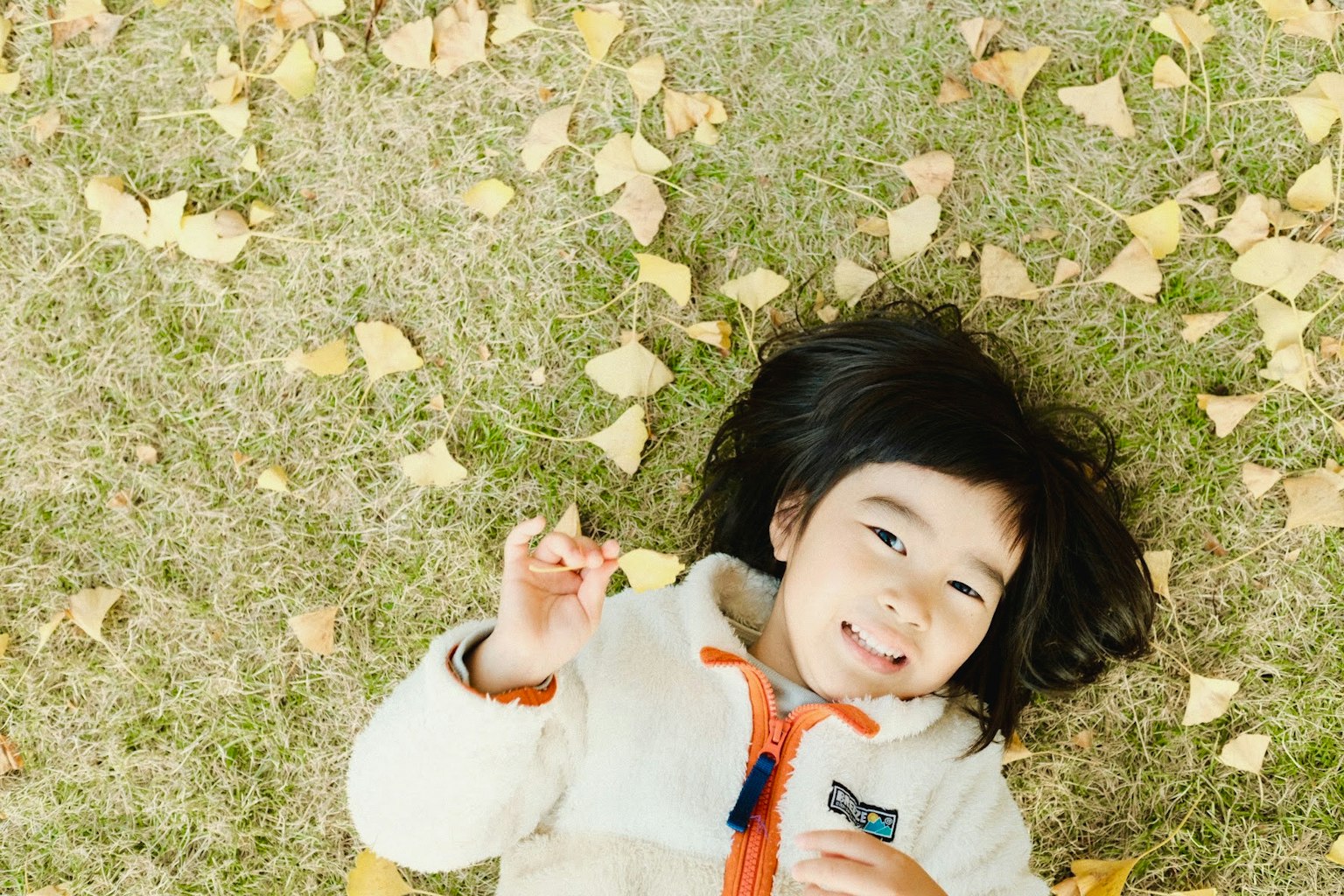 草の上に寝転がる子供の笑顔と秋の葉
