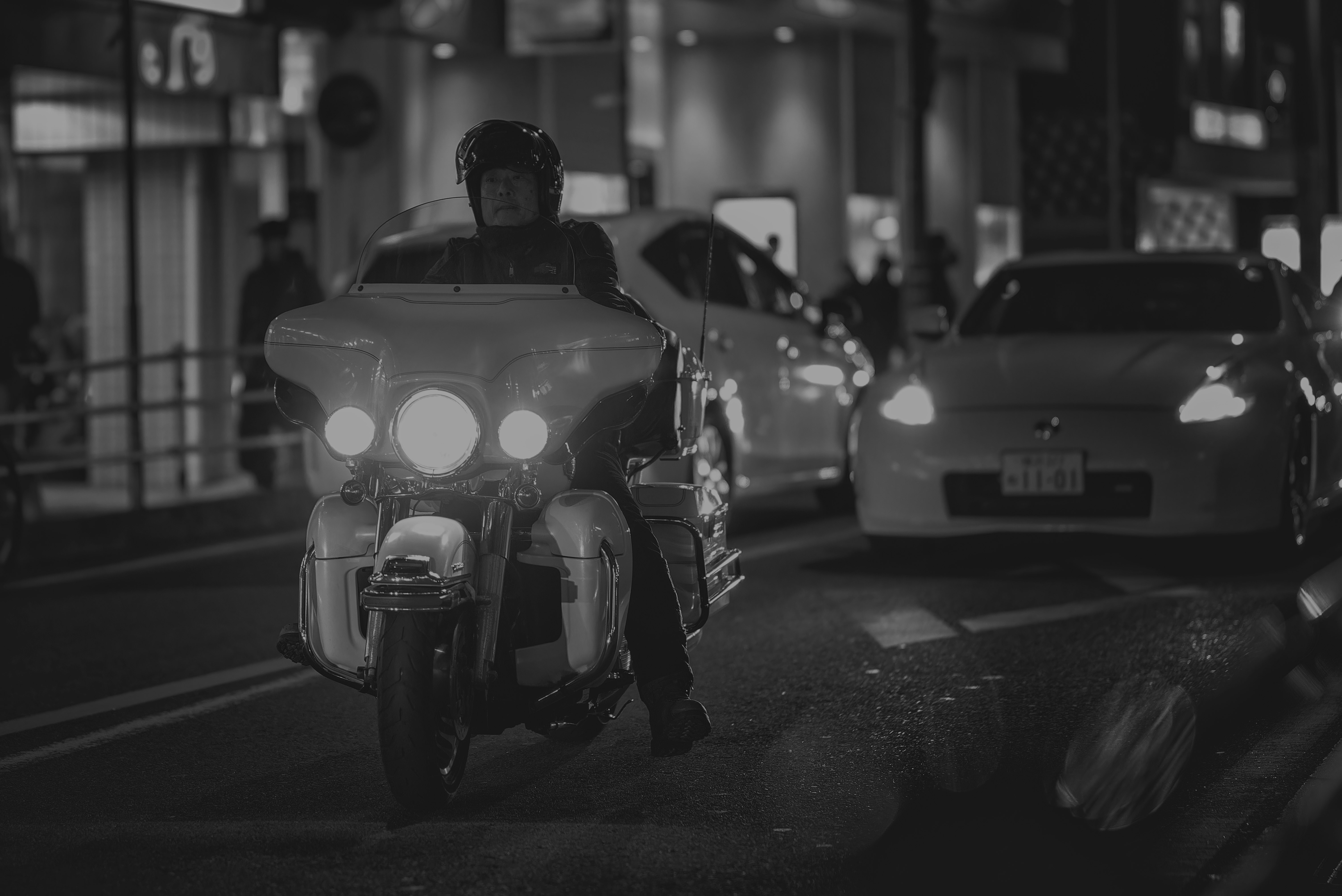 夜の路地でライトを点けたバイクと車が並ぶ街並み