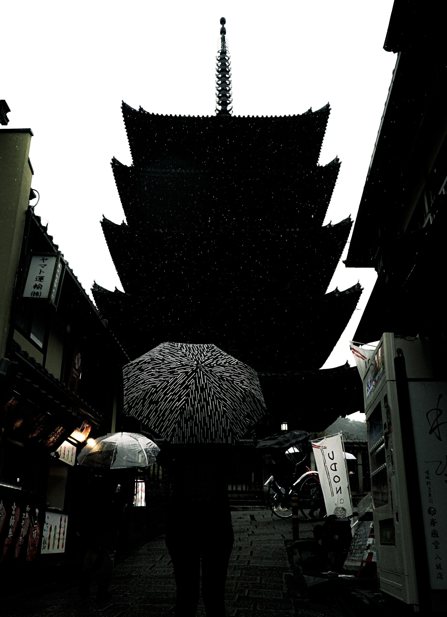 Silhouette pagoda dengan seseorang memegang payung di bawah hujan