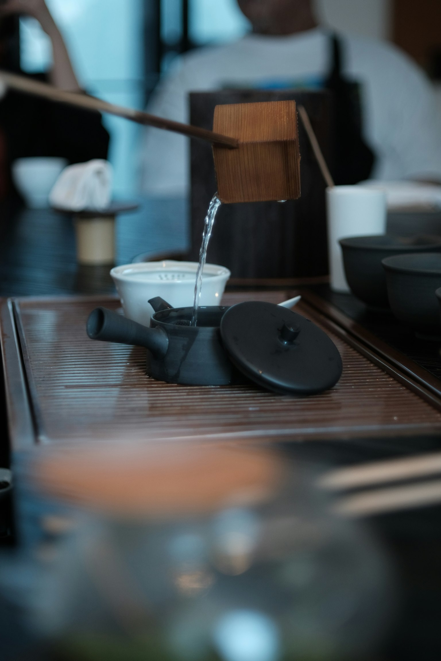 กาน้ำชากำลังเทชาลงในชามบนโต๊ะไม้พร้อมอุปกรณ์ชาที่หลากหลาย