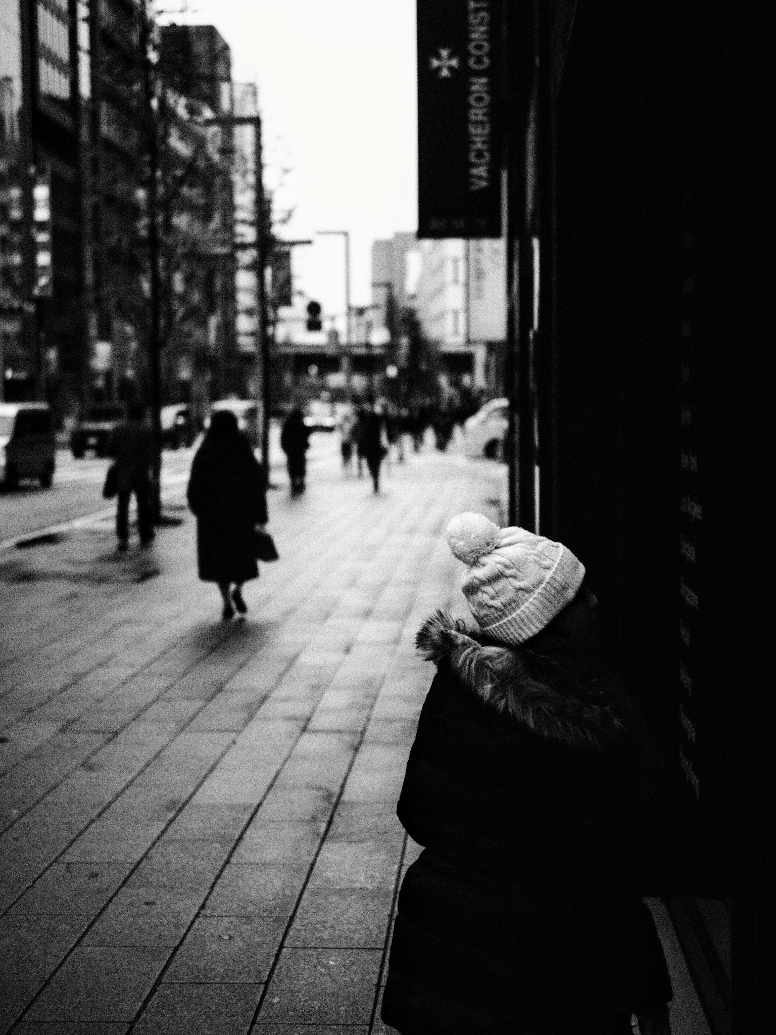 Kind mit weißer Mütze auf einer Stadtstraße mit Fußgängern in Silhouette