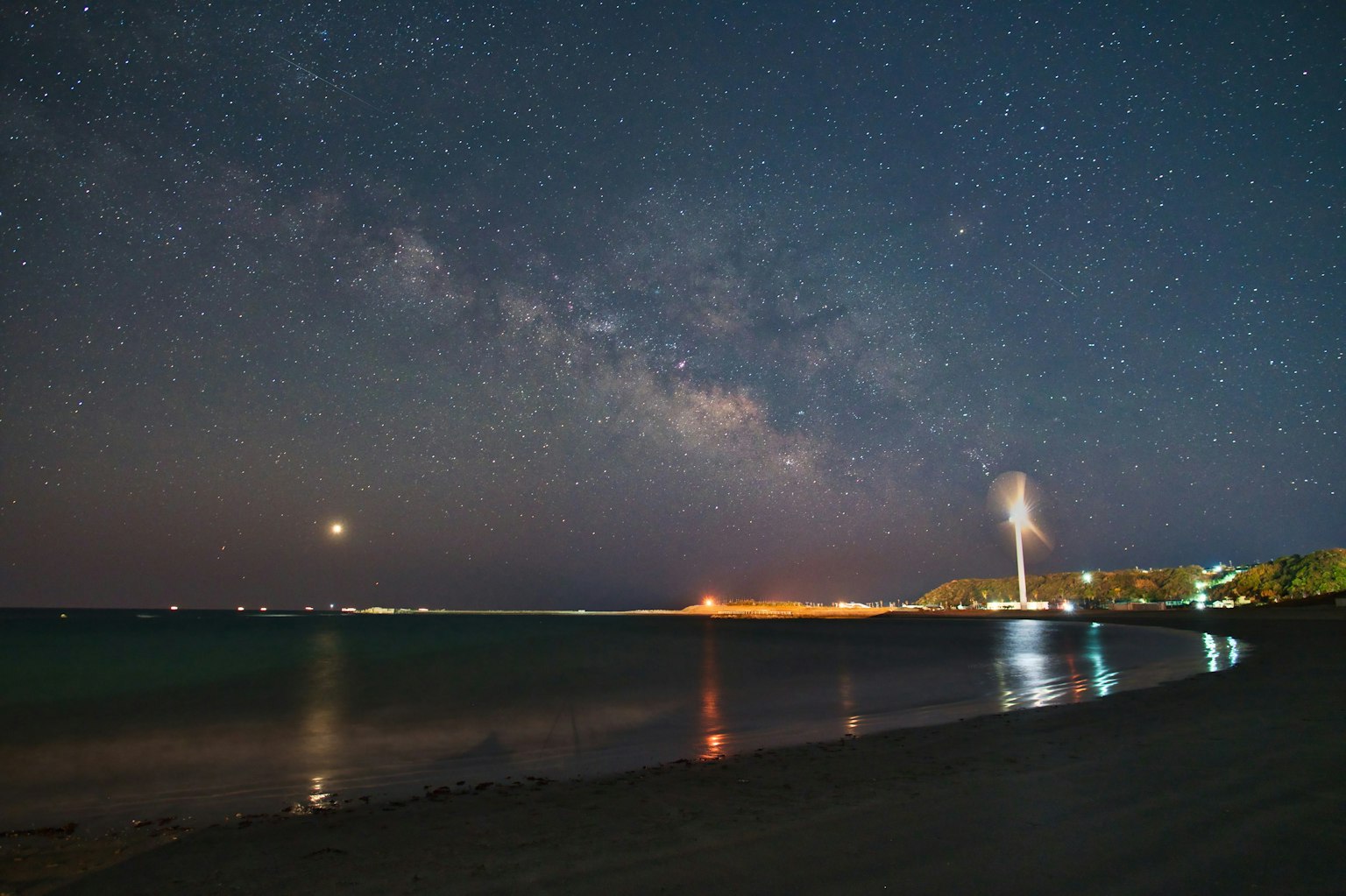 Galaksi Bima Sakti di atas garis pantai dengan ombak tenang di bawah langit berbintang