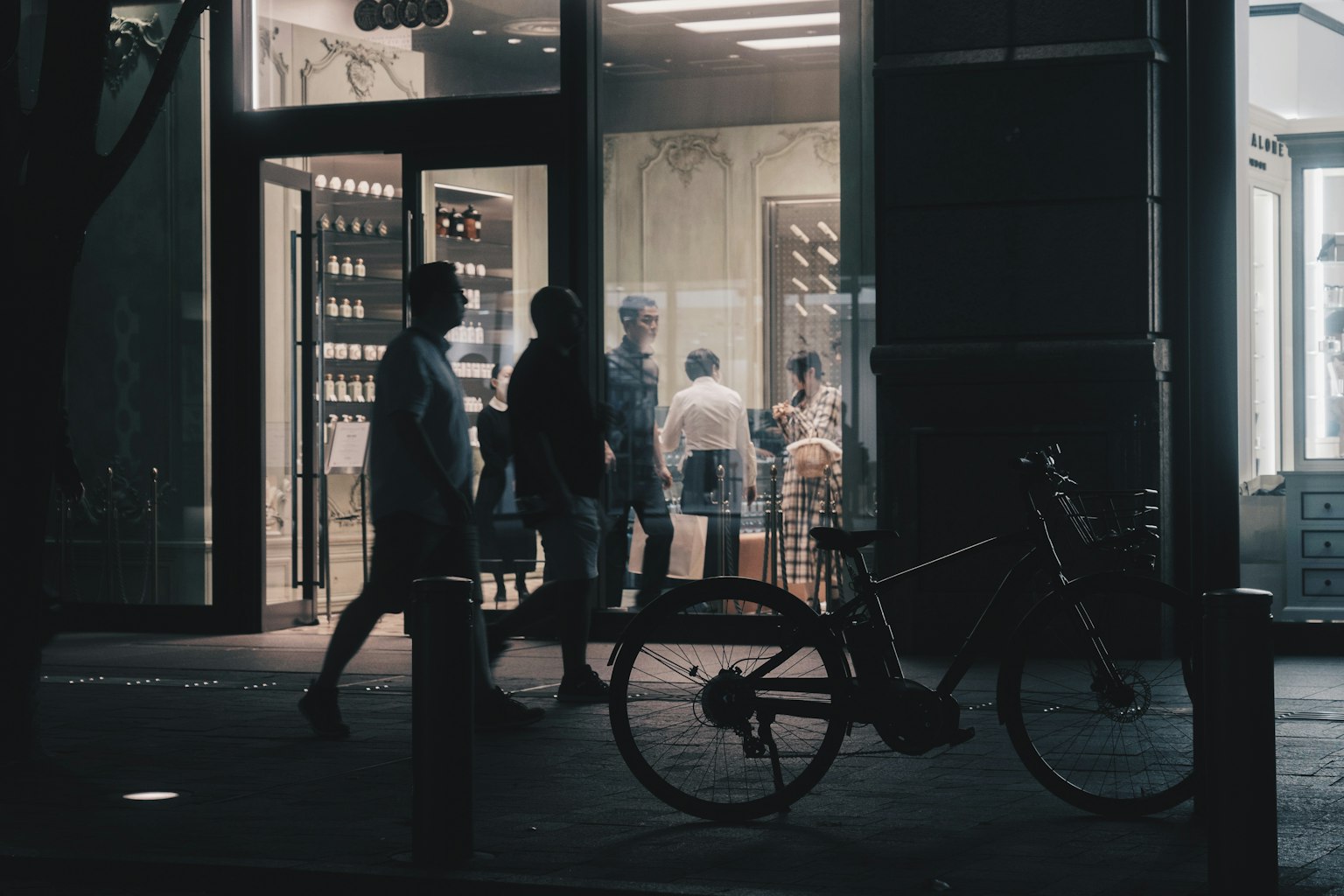 Silhouetten von Fußgängern, die an einem Geschäft vorbeigehen, mit einem Fahrrad im Vordergrund