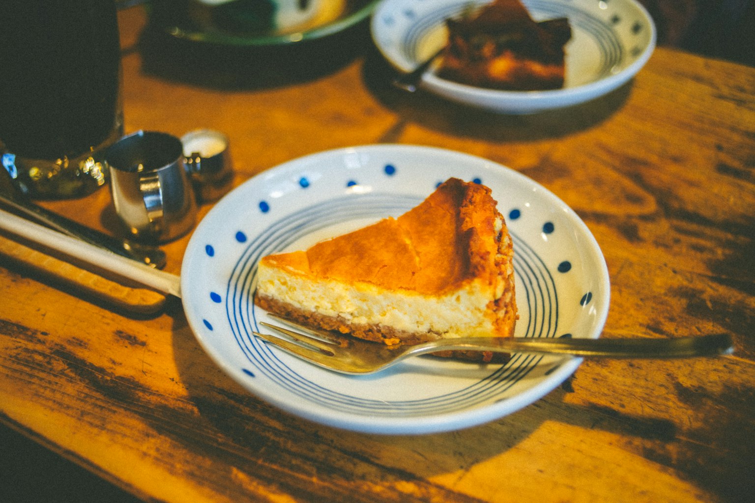Miếng cheesecake trên đĩa trắng có chấm xanh trên bàn gỗ
