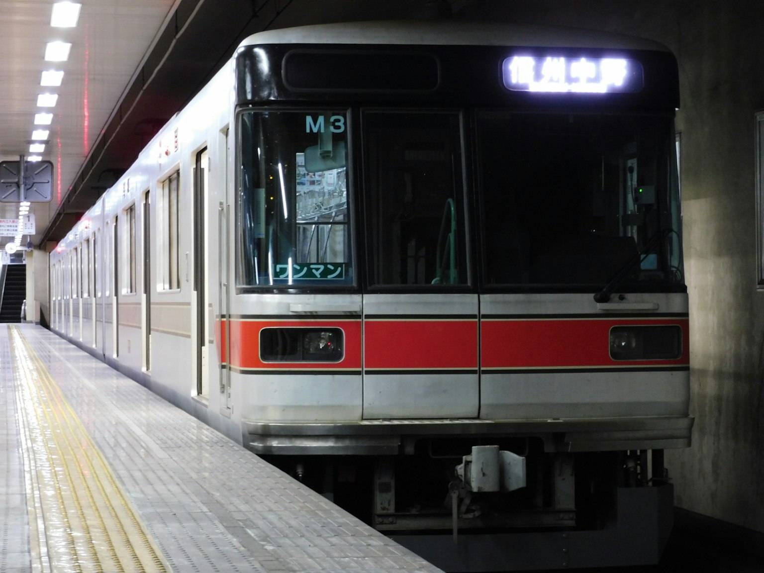 Subway train stopped at the station featuring red stripe