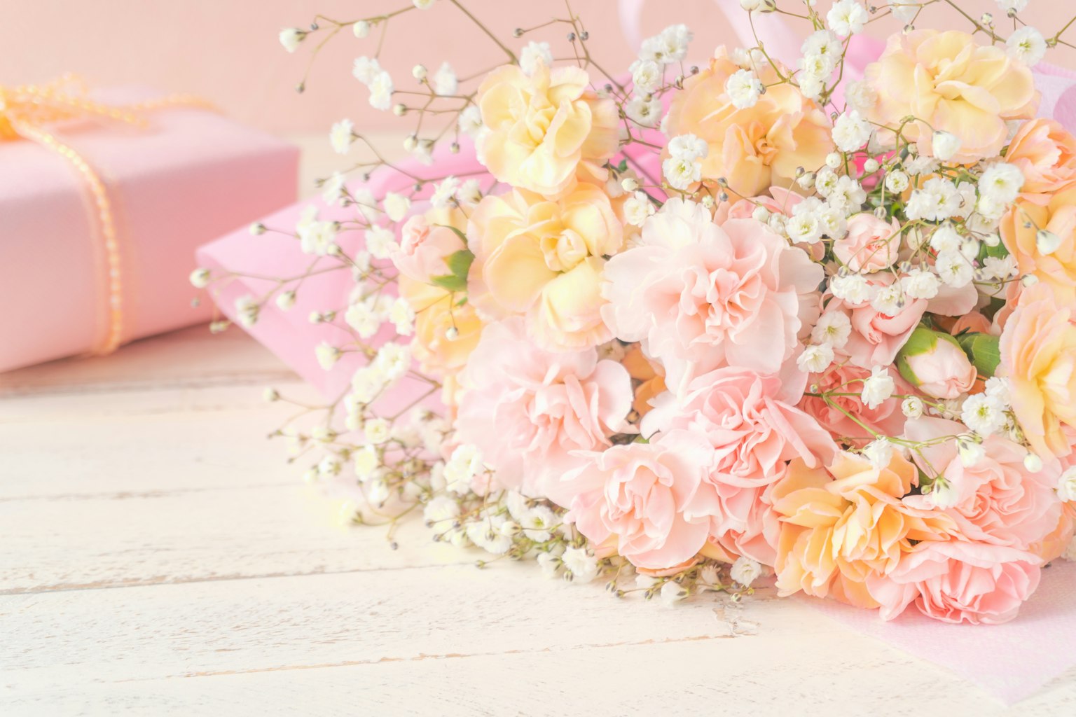 Un ramo de flores rosas y naranjas con una caja de regalo al fondo