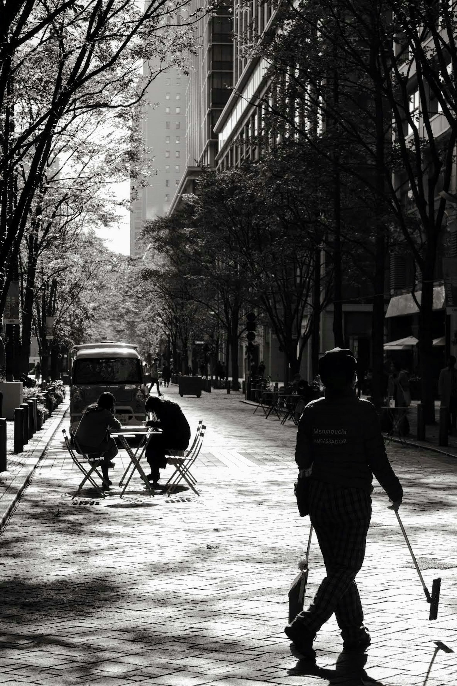 Silhouette d'une personne marchant dans la rue avec deux assis à une table