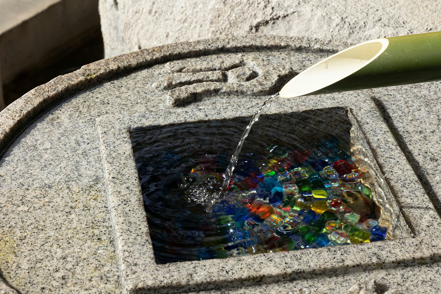 Bañera de piedra con agua fluyendo de bambú y piedras de vidrio coloridas