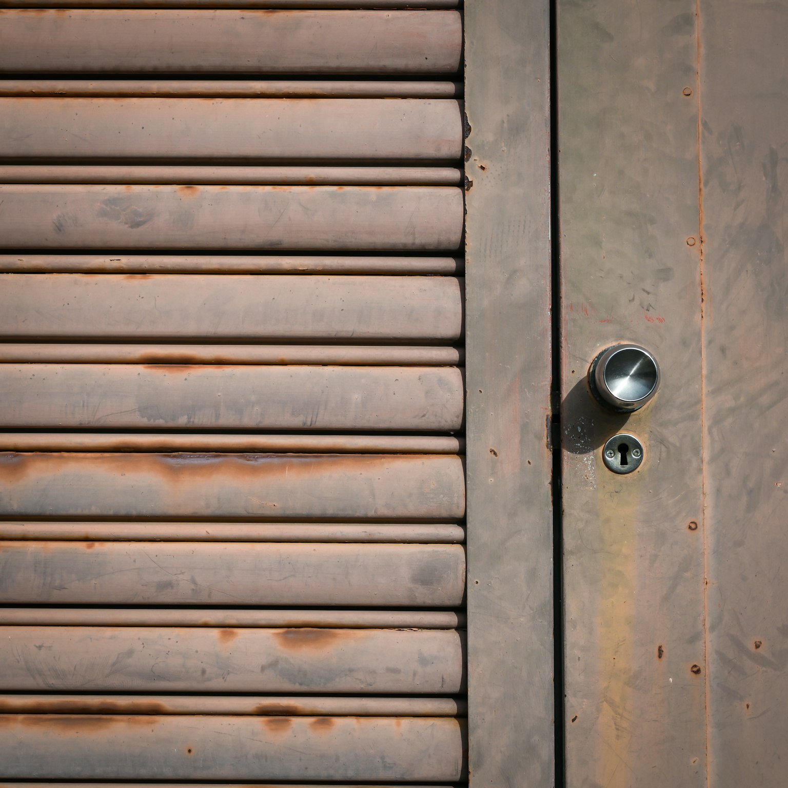 Tampilan dekat pintu logam berkarat dengan slat horizontal dan knop logam