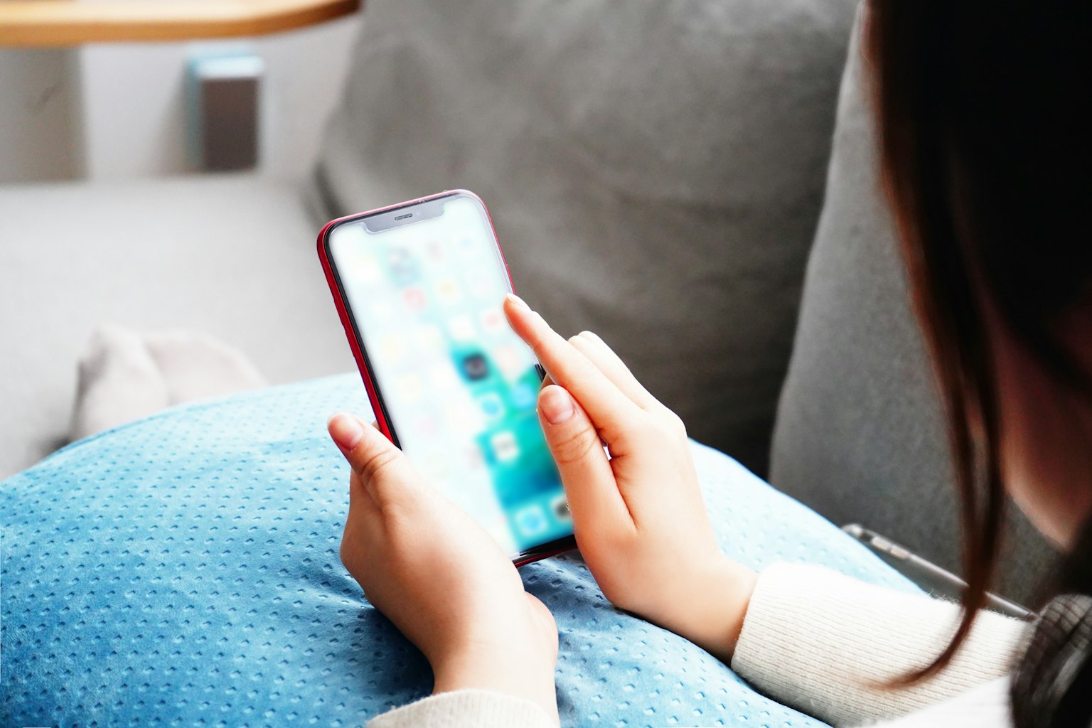 A person's hands using a smartphone while sitting on a couch