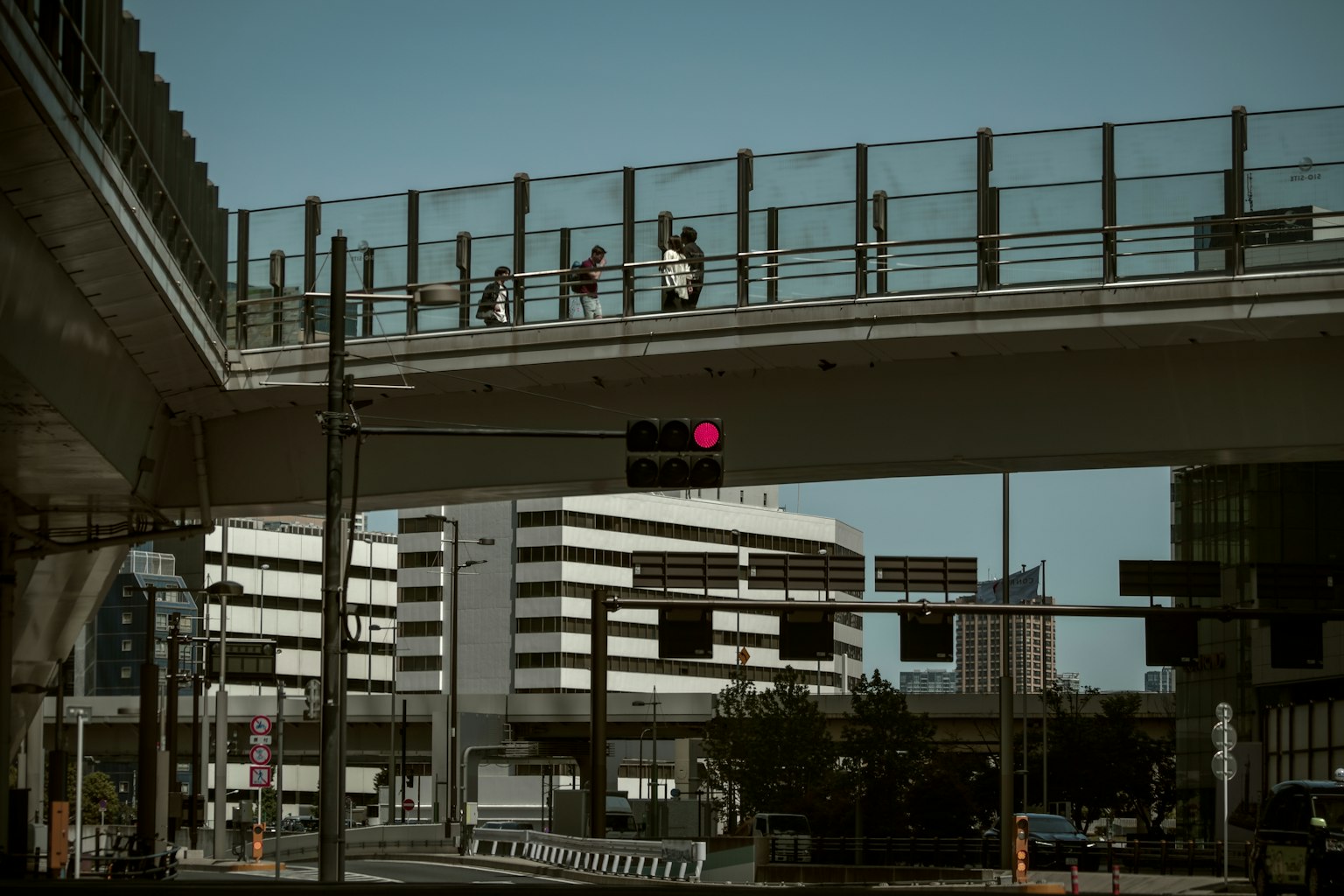 Escena urbana con personas caminando en un paso elevado y un semáforo en rojo