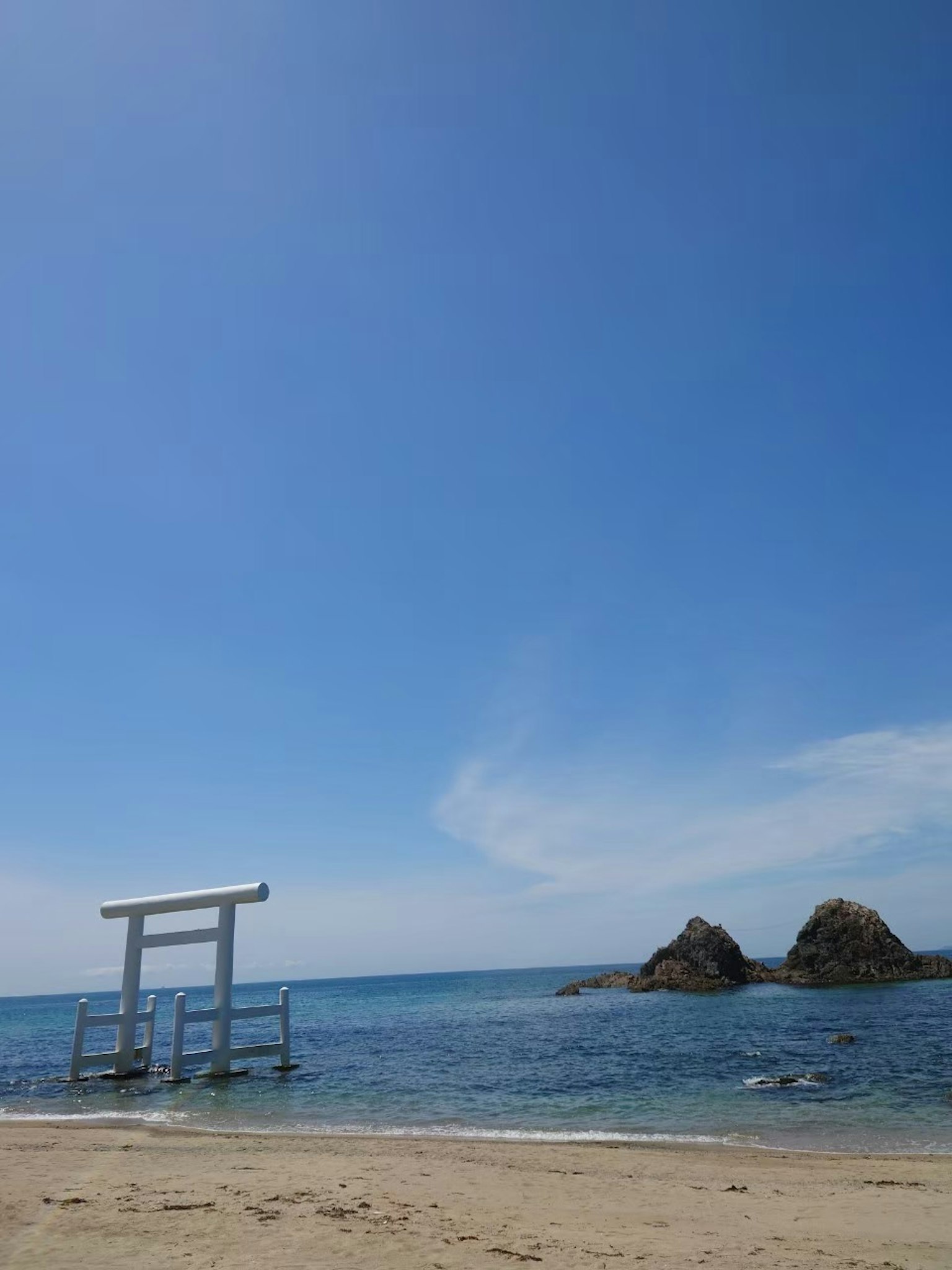 Scena costiera con un torii e rocce sotto un cielo blu chiaro